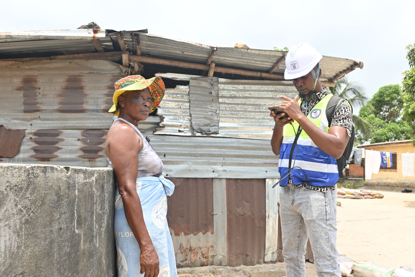 A WaterStep inspector records a hand pump on his phone while a community member looks on, Liberia